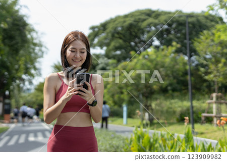 Young beautiful woman sportswear workout clothes using smartphone and listening to music with headphones standing relax in park during exercise blue sky background. fitness healthy concept. 123909982