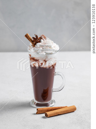 Hot chocolate with whipped cream, cinnamon and spices in a tall glass on a light background. 123910138