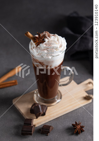 Hot chocolate with whipped cream, cinnamon and spices in a tall glass on a dark background. 123910140