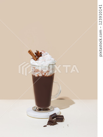 Hot chocolate with whipped cream, cinnamon and spices in a tall glass on a white beige background Hot chocolate with whipped cream, cinnamon and spices in a tall glass on a white beige background 123910141