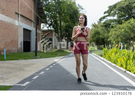 Young beautiful woman sportswear workout clothes using smartphone and listening to music with headphones standing relax in park during exercise blue sky background. fitness healthy concept. 123910176