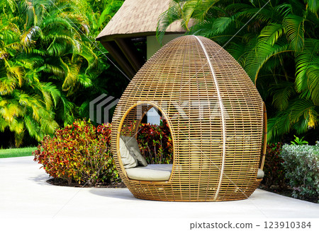Egg-shaped cozy wicker lounge bed in a tropical garden 123910384