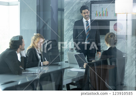 Team members collaborate in bright office space, discussing data and project strategies while leader presents insights on screen, fostering innovation and teamwork. 123910585