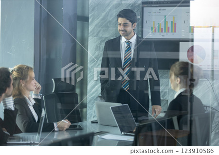 Team members collaborate in bright office space, discussing data and project strategies while leader presents insights on screen, fostering innovation and teamwork. 123910586