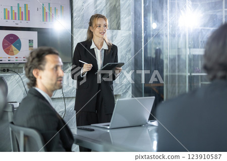 business professional presents data analysis findings in sleek, modern office setting while colleagues attentively listen. Bright charts and graphs enhance atmosphere. business professional presents data analysis findings in sleek, modern office setting while colleagues attentively listen. Bright charts and graphs enhance atmosphere. 123910587