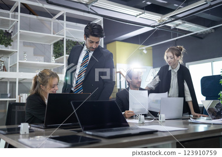 Four professionals engage in a collaborative discussion in a contemporary office space, analyzing documents and sharing insights while seated at a conference table. 123910759