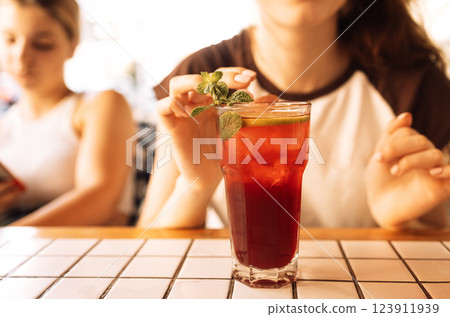 Close-up of a glass with a delicious chilled cocktail with mint and lime on the table. A girl is drinking a Tasty citrus drink with ice in a cafe inside. Close-up of a glass with a delicious chilled cocktail with mint and lime on the table. A girl is drinking a Tasty citrus drink with ice in a cafe inside. 123911939