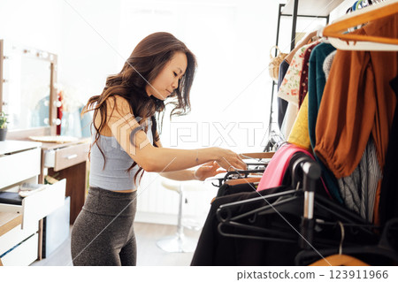 An attractive Asian woman chooses her clothes in the dressing room at home. A cute Korean girl in a gray top and leggings is changing in the bedroom. 123911966