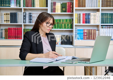 Middle aged female teacher working inside library office with laptop 123912046