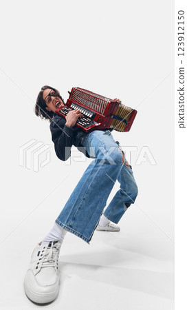 Dynamic low angle view of man, accordionist in ripped jeans bending back, performing with explosive energy and expressive movement. 123912150