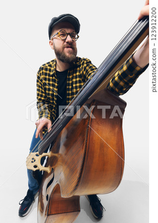 Bearded man in checkered shirt passionately playing double bass, leaning into the rhythm with intense expression against white background. Bearded man in checkered shirt passionately playing double bass, leaning into the rhythm with intense expression against white background. 123912200