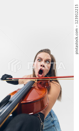 Emotional young woman with exaggerated emotions, fully immersed in electrifying violin performance, changing classical artistry Emotional young woman with exaggerated emotions, fully immersed in electrifying violin performance, changing classical artistry 123912215