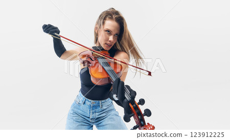 Passionate young woman, musician gripping violin with intensity, playing with energy and freedom against white background. 123912225