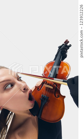 Funny close-up image of expressive young woman, violinist dramatically reacting to bow strokes, transforming classical elegance into theatrical expression. 123912226