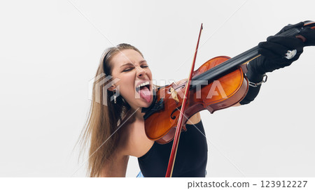 Expressive young woman violinist sticking out tongue, breaking classical norms, making passionate performance, playing violin against white background Expressive young woman violinist sticking out tongue, breaking classical norms, making passionate performance, playing violin against white background 123912227