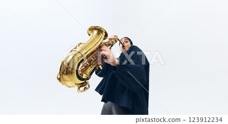 Low-angle view of female musician emotionally playing saxophone, fully lost in melody and performance against white background. Low-angle view of female musician emotionally playing saxophone, fully lost in melody and performance against white background. 123912234