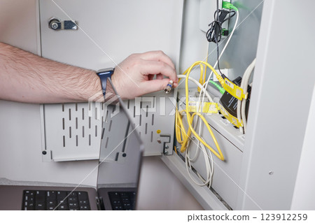 technician installing network cable in server cabinet while configuring internet connection for IT infrastructure technician installing network cable in server cabinet while configuring internet connection for IT infrastructure 123912259