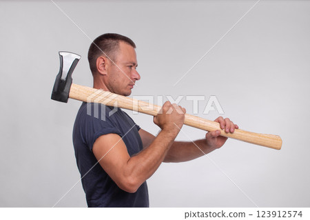 A man with an axe stands against a grey background, captured in a side view. The image emphasizes the man's strength and the axe's sharpness, creating a powerful and dynamic composition. concept 123912574