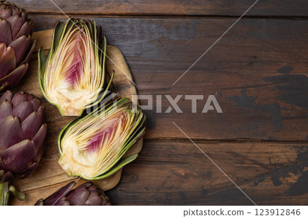 Halves and whole purple raw roman artichokes on a dark wooden table top view. Fresh italian vegetables 123912846