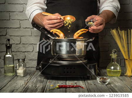 A chef expertly adds spices to a pot while cooking chicken feet broth, surrounded by ingredients in a well-equipped kitchen. Warm lighting enhances the culinary atmosphere 123913585
