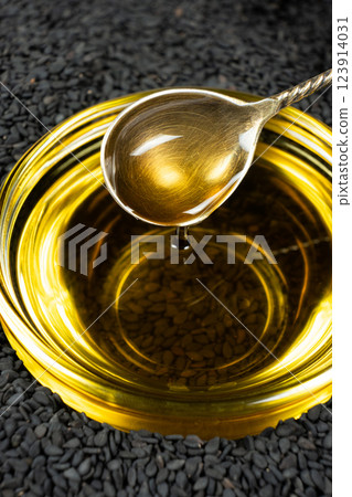 Black sesame oil poured from a spoon into a glass bowl 123914031
