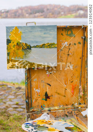 Autumn landscape painting on canvas displayed on an easel by a lake outdoors 123914062