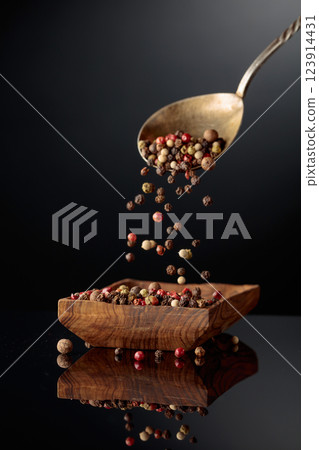Black, red, white, and allspice peppercorns is poured in wooden dish. 123914431
