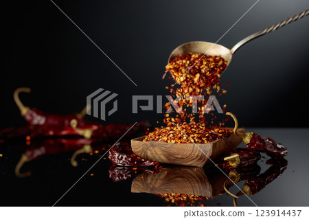 Dry red chili peppers and crushed chili flakes on a black reflective background. Dry red chili peppers and crushed chili flakes on a black reflective background. 123914437
