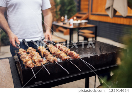 Close-up of male hands holding skewers with meat. A man cooks juicy and tasty pieces of meat baked on coals. Delicious fresh barbecue on an outdoor campfire. 123914634