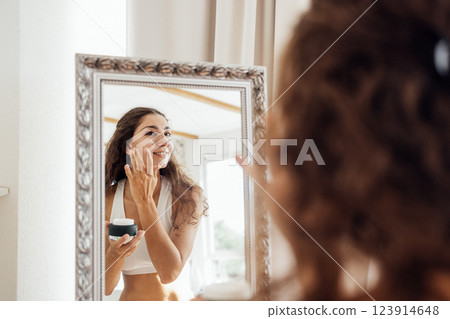 Young attractive woman looks in mirror and applies face cream. 123914648