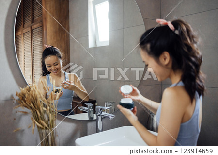 Asian young woman applies moisturizing cream to her face Asian young woman applies moisturizing cream to her face 123914659