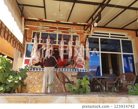 A man stands in front of a butcher shop with meat hanging 123914742