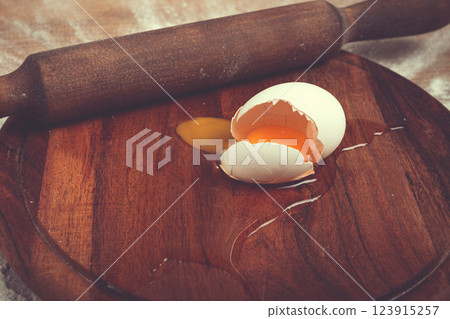 Broken egg and rolling pin on wooden board in kitchen setting during food preparation Broken egg and rolling pin on wooden board in kitchen setting during food preparation 123915257