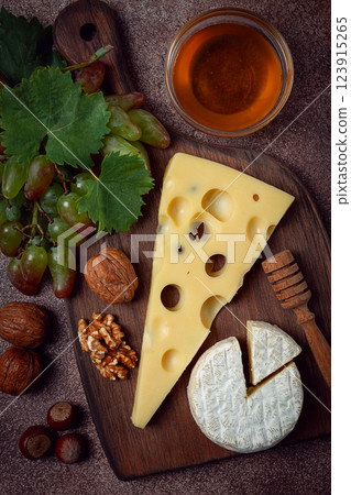 cheese with big holes, emmental, maasdam, brie cheese, on a cutting board, with grapes and honey, nuts, appetizer to wine, top view, 123915265