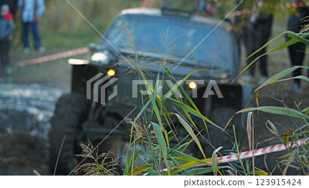 On a background of green grass, an off-road vehicle is seen ruggedly driving along a muddy track during a competition. Extreme mud racing 123915424