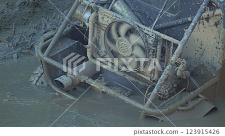 Close-up of a muddy off-road vehicle stuck in deep mud. The radiator fan installed in the rear of the car is rotating. Extreme mud racing 123915426