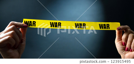 Hands Holding Yellow Tape With War Text On Black Background Hands Holding Yellow Tape With War Text On Black Background 123915495