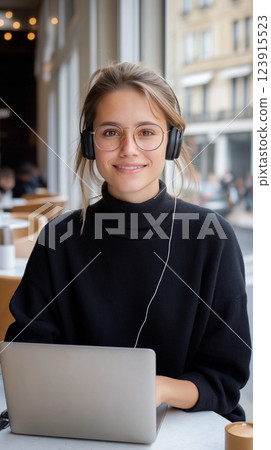 young woman with headphones smiles while working on laptop in cafe young woman with headphones smiles while working on laptop in cafe 123915523