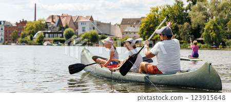 Man with two children enjoy having fun paddling canoe rent across lake river water wearing bright orange life vests hot sunny summer day. Healthy recreational activity lifestyle vacation trip journey 123915648
