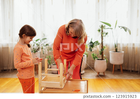 Elderly woman in casual clothes and her little granddaughter are assembling new wooden chair 123915923