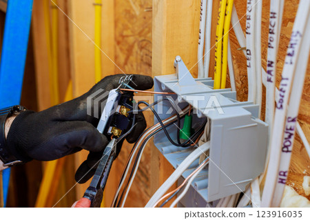 Electrician contractor wearing gloves connects wires to switch light, installation in new home under construction. 123916035