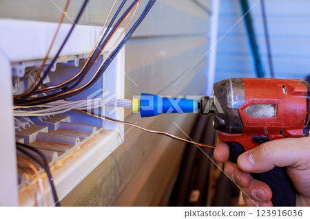 An electrician works on connecting several wires outside, focused on his task with screwdriver tool in hand. 123916036