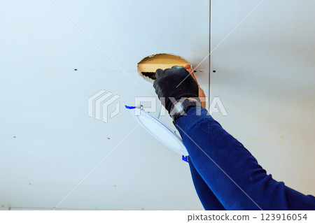 Electrician connects wires led lamp at ceiling while renovating home, ensuring proper electrical setup 123916054