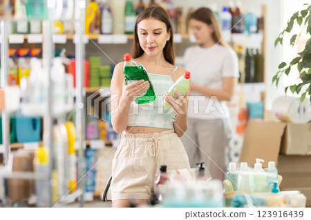 Female shopper chooses dishwashing at home goods store, while in background shoppers browse products Female shopper chooses dishwashing at home goods store, while in background shoppers browse products 123916439
