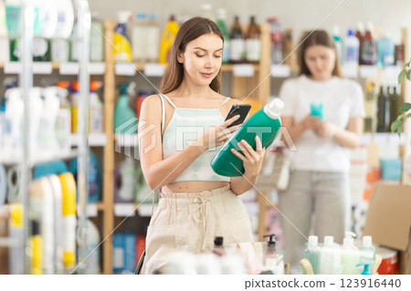 Woman scans QR code on label of detergent using her smartphone, while in background shoppers browse products 123916440