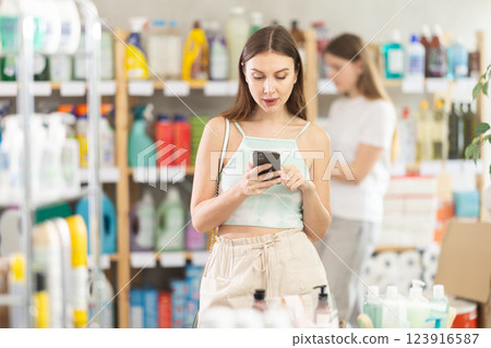 Woman checking the list on her smartphone in supermarket. In background shoppers browse products Woman checking the list on her smartphone in supermarket. In background shoppers browse products 123916587
