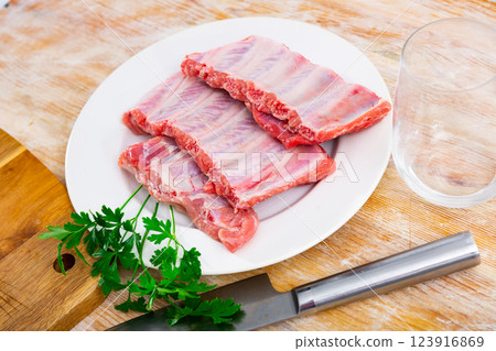 Unprepared pork ribs chopped and ready-to-cook served on white plate decorated with parsley 123916869