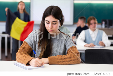 Teenage students sitting in class and listening carefully to female teacher holding Belgian flag 123916992