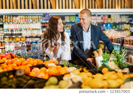 Glad couple is standing with cart with products in supermarket Glad couple is standing with cart with products in supermarket 123917003