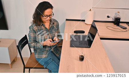 Woman Using Smartphone and Laptop at Home Workspace with Coffee 123917015